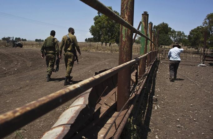 Nadav (R), the chief cowboy of the Yonatan herd, walks next to Israeli soldiers on a ranch just outside Moshav Yonatan, a collective farming community, about 2 km (1 mile) south of the ceasefire line between Israel and Syria in the Golan Heights May 21, 2013. The group of cowboys, who have been running the ranch on the Golan's volcanic rocky plateau for some 35 years, also host the Israeli military, who use half of the cattle farm, 20,000 dunams (5,000 acres), as a live-fire training zone. Israel captured the Golan Heights from Syria in the 1967 Middle East war and annexed the territory in 1981, a move not recognized internationally. Picture taken May 21, 2013. REUTERS/Nir Elias (ENVIRONMENT ANIMALS SOCIETY) ATTENTION EDITORS: PICTURE 14 OF 27 FOR PACKAGE 'COWBOYS GOLAN HEIGHTS' SEARCH 'COWBOY GOLAN' FOR ALL Published: Kvě. 29, 2013, 10:06 dop.