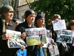 Ženy před soudní síní ve Vladikavkazu drží fotografie obětí beslanského útoku. Žena drží nápis: "Kulajeve a tobě podobní, budete prokletí na věky"