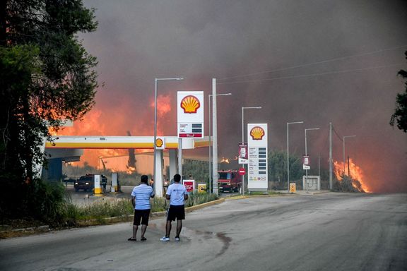 Lidé sledují, jak poblíž čerpací stanice v Achaji v Řecku hoří lesní požár.