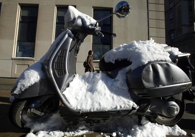 A woman walks past a snow covered Vespa in New York, February 9, 2013. A blizzard pummelled the Northeastern United States, killing at least one person, leaving hundreds of thousands without power and disrupting thousands of flights, media and officials said. REUTERS/Carlo Allegri (UNITED STATES - Tags: ENVIRONMENT) Published: Úno. 10, 2013, 12:15 dop.