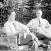 Bratří Čapkové, Karel Čapek, spisovatel (vlevo) a Josef Čapek, malíř, sedí na zahradě v křesle, na klíně mají foxteriéry.psa.