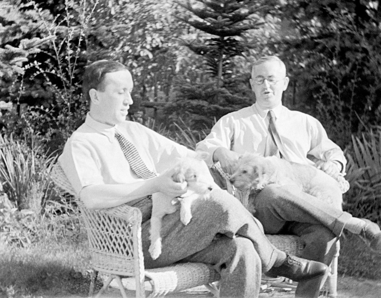 Bratří Čapkové, Karel Čapek, spisovatel (vlevo) a Josef Čapek, malíř, sedí na zahradě v křesle, na klíně mají foxteriéry.psa.