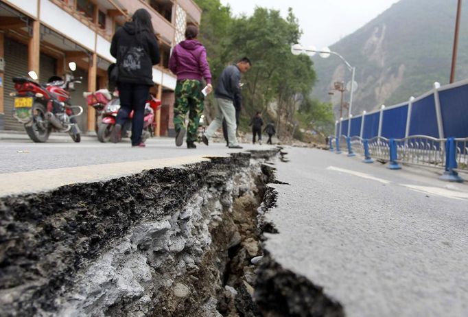 People walk next to a crack on the road after Saturday's earthquake in Baoxing county, Sichuan province, April 21, 2013. Rescuers struggled to reach a remote, rural corner of southwestern China on Sunday as the death toll climbs to 186 people dead and 11,393 injured, Xinhua News Agency reported. Picture taken April 21, 2013. REUTERS/China Daily (CHINA - Tags: DISASTER) CHINA OUT. NO COMMERCIAL OR EDITORIAL SALES IN CHINA Published: Dub. 22, 2013, 3:06 dop.