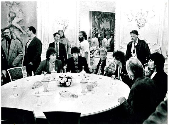 Václav Havel s Rolling Stones sedí u stolu, ve stoje zleva Ladislav Kantor, Karel Schwarzenberg, ochranka, Lubomír Schmidtmajer, Vladimír Hanzel, tlumočník Michal Staša.