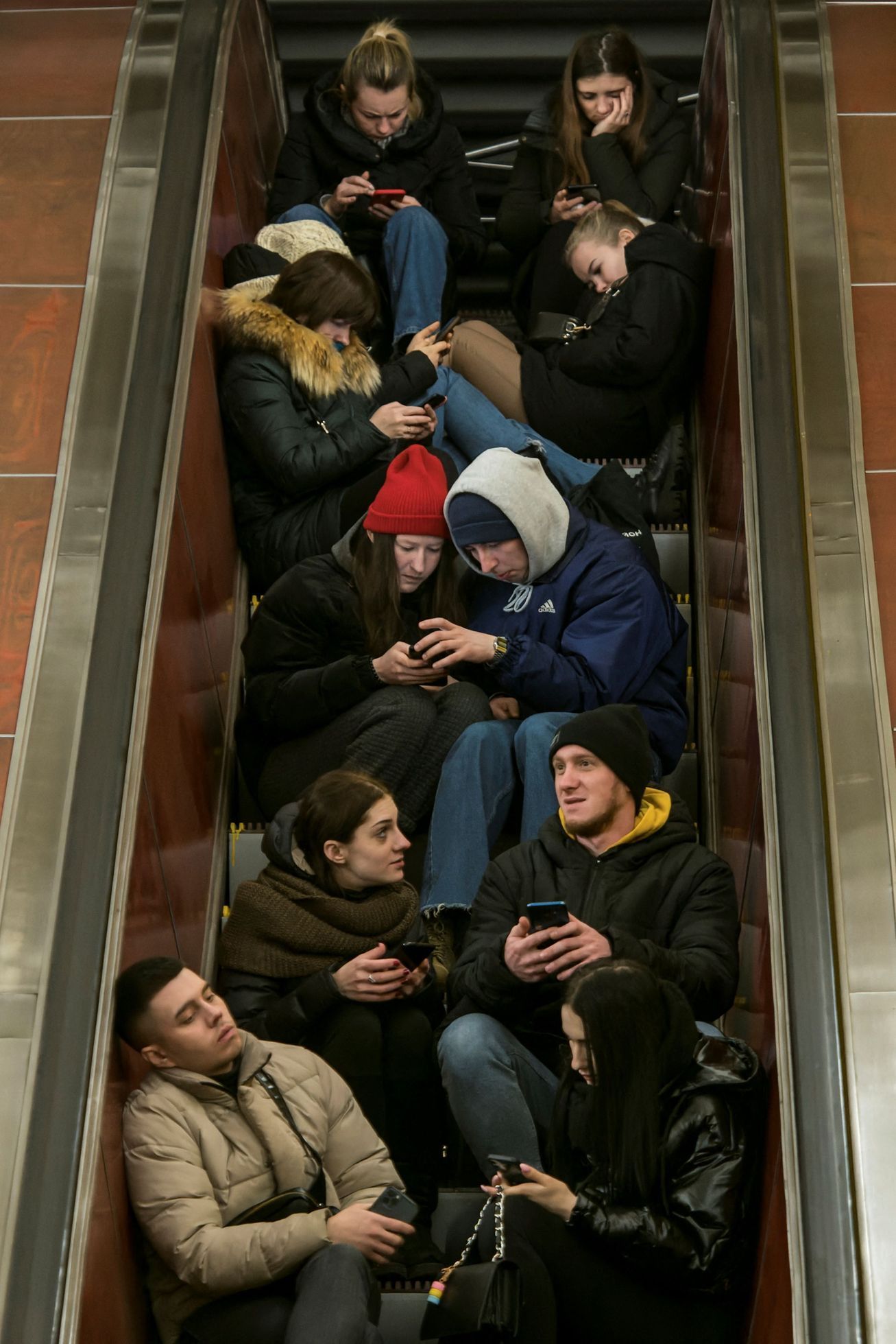 Lidé sedí na eskalátoru v kyjevském metru, které používají v době ruského bombardování jako kryt.