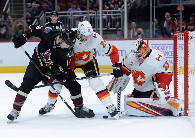 NHL 2019/20, Arizona - Calgary: Christian Dvorak (Arizona) a Travis Hamonic (Calgary) bojují o puk před brankářem Davidem Rittichem.