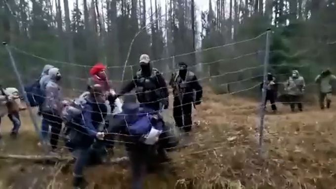Běloruští ozbrojení vojáci násilně tlačí migranty včetně žen a dětí přes plot do Polska.
