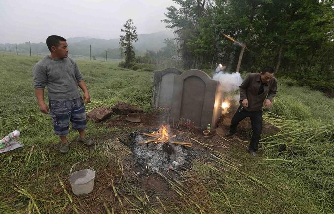 A man dodges after lighting firecrackers in front of the tomb of his friend's (L) father, who died during Saturday's earthquake in Lushan county, Ya'an, Sichuan province, April 23, 2013. Burning firecrackers during a burial for relatives is believed to dispel evil spirits away from the dead, in some parts of China. Picture taken April 23, 2013. REUTERS/Stringer (CHINA - Tags: DISASTER SOCIETY OBITUARY) CHINA OUT. NO COMMERCIAL OR EDITORIAL SALES IN CHINA Published: Dub. 24, 2013, 4:49 dop.