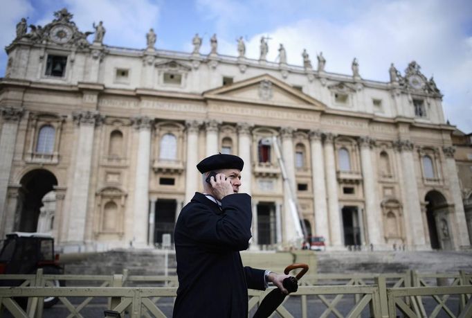 A priest chats on his phone as he watches workers put up a red curtain on the central balcony, called the Loggia of the Blessings of Saint Peter's Basilica at the Vatican March 11, 2013. After being elected in the conclave the new pope will appear on the balcony. REUTERS/Dylan Martinez (VATICAN - Tags: RELIGION) Published: Bře. 11, 2013, 10:20 dop.