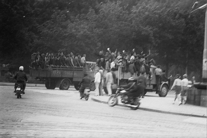 Protestní jízda lidí na náklaďácích a motorkách projíždí přes dnešní Moravské náměstí, dříve náměstí Rudé armády. Nápis na bočnici druhého vozu: "Ať žije svoboda!"