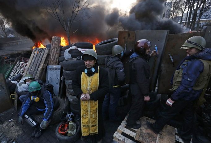 Anti-government protesters and a priest look out from a barricade in Kiev February 21, 2014.