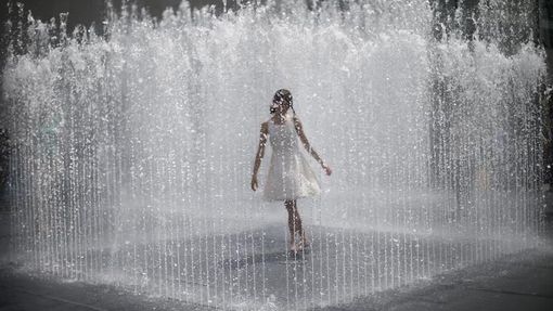 Dívka obklopená tryskající vodou z fontány na South Bank během horkého letního dne v centru Londýna. 15. července 2013.