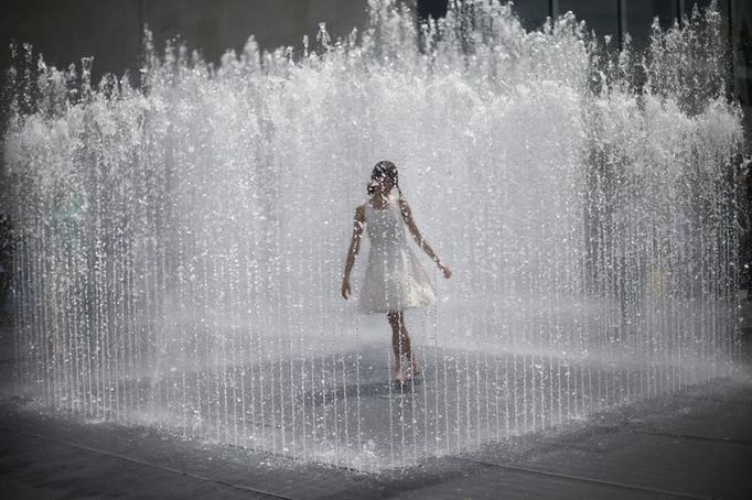 Dívka obklopená tryskající vodou z fontány na South Bank během horkého letního dne v centru Londýna. 15. července 2013.