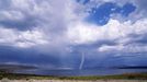 A storm and tornado form over water in a desert landscape