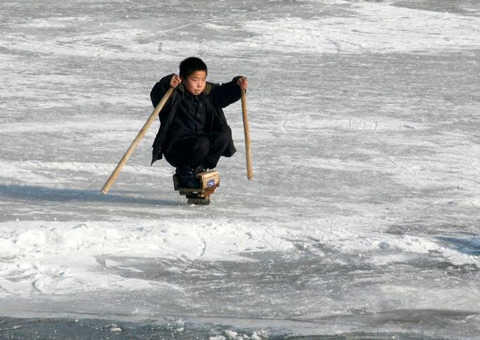 Malý, severní Korejec se prohání po zamzlé řece Yalu na dřevěných bruslích.