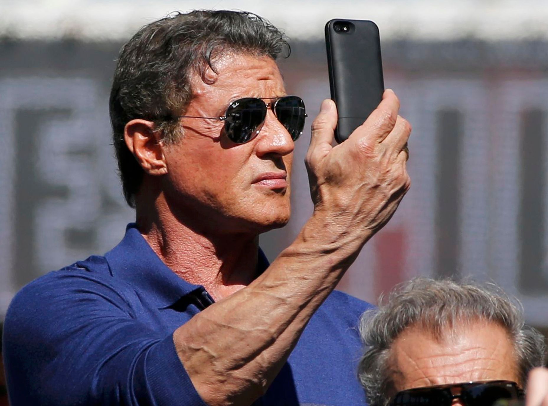 Cast member Sylvester Stallone holds a mobile phone as he poses on a tank arriving on the Croisette to promote the film &quot;The Expendables 3&quot; during the 67th Cannes Film Festival in Cannes