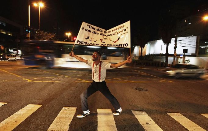 A member of the group Traffic Psychologists performs as he holds up a banner in front of traffic light in Sao Paulo July 23, 2012. Traffic Psychologists is a non-profit non-governmental organization which aims to humanize traffic and reduce the level of stress caused to drivers. Sao Paulo has more than 7 million vehicles, according to figures from the state transport authority Detran. The banner reads "A day without laughter is a day wasted". Picture taken July 23, 2012. REUTERS/Nacho Doce (BRAZIL - Tags: TRANSPORT SOCIETY) Published: Čec. 24, 2012, 6:54 dop.