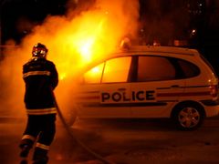 Požárník hasí auto při nepokojích na severu Paříže.