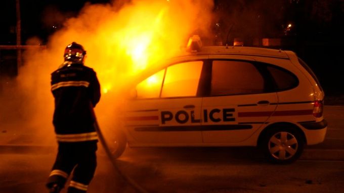 Požárník hasí auto při nepokojích na severu Paříže.