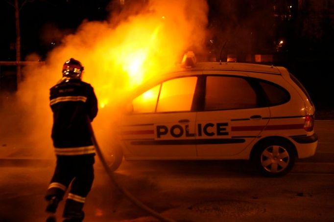 Požárník hasí auto při nepokojích na severu Paříže.