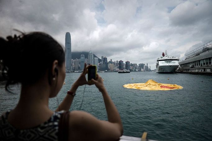 A woman takes a picture of the 16.5-metre-tall inflatable Rubber Duck art installation as it lies deflated in Hong Kong's Victoria Harbour on May 15, 2013. Organisers said the inflatable Rubber Duck created by Dutch artist Florentijn Hofman had been deflated for scheduled maintenance, but visitors who had made the trip to see it were left disappointed.