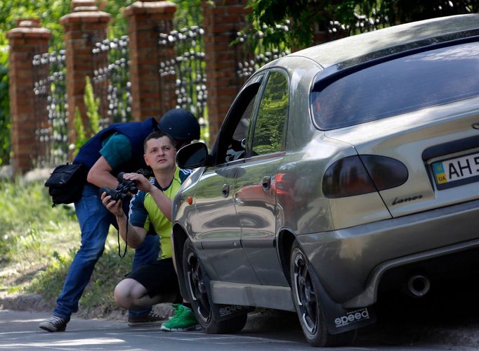 Fotoreportér a jeden z místních obyvatel se kryjí za autem během bojů o doněcké letiště. (26. května 2014)