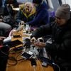 Lidé v Kyjevě si dobíjejí mobili na veřejném místě, kde elektřinu zajišťuje generátor.