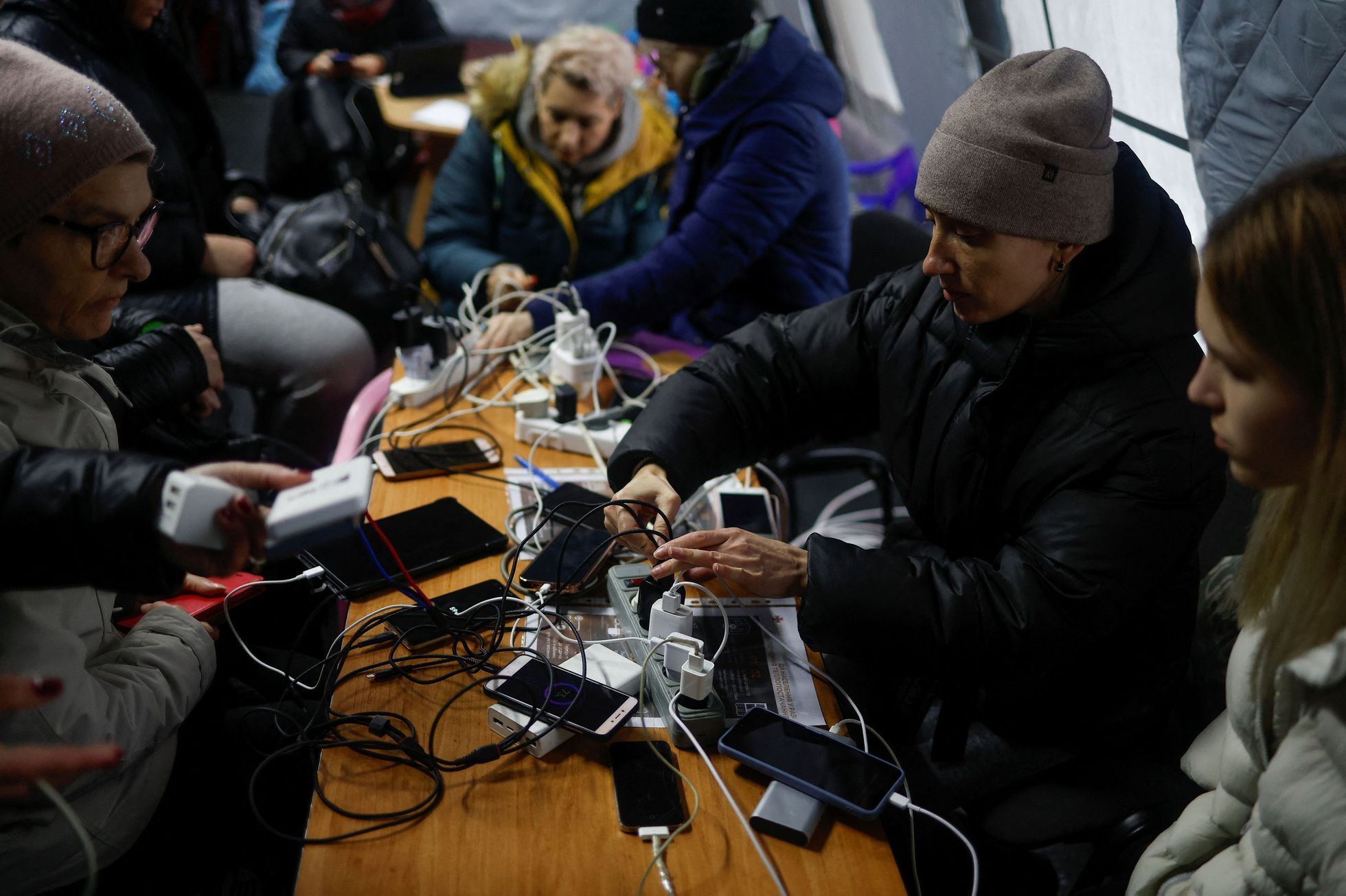Lidé v Kyjevě si dobíjejí mobili na veřejném místě, kde elektřinu zajišťuje generátor.
