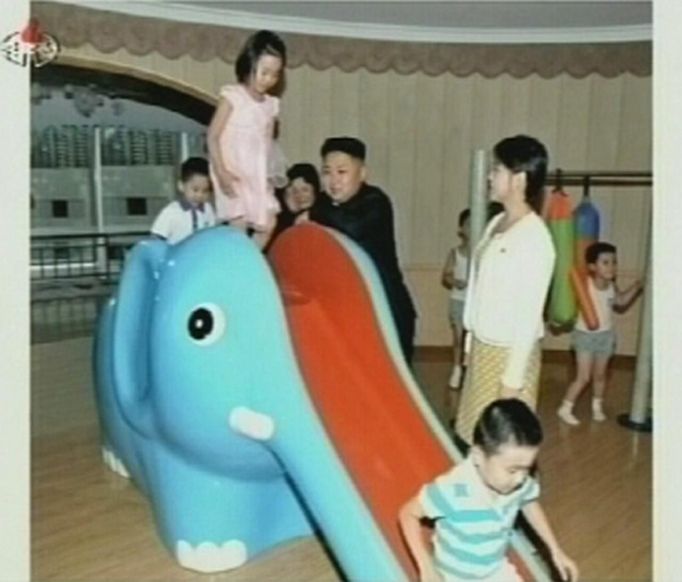 North Korean leader Kim Jong-un watches children playing on a slide, as an unidentified woman stands near him, during a visit to a pre-school in Pyongyang in this undated still image aired on video. REUTERS/KRT via Reuters TV (NORTH KOREA - Tags: POLITICS) FOR EDITORIAL USE ONLY. NOT FOR SALE FOR MARKETING OR ADVERTISING CAMPAIGNS. THIS IMAGE HAS BEEN SUPPLIED BY A THIRD PARTY. IT IS DISTRIBUTED, EXACTLY AS RECEIVED BY REUTERS, AS A SERVICE TO CLIENTS. NORTH KOREA OUT. NO COMMERCIAL OR EDITORIAL SALES IN NORTH KOREA Published: Čec. 15, 2012, 5:54 dop.