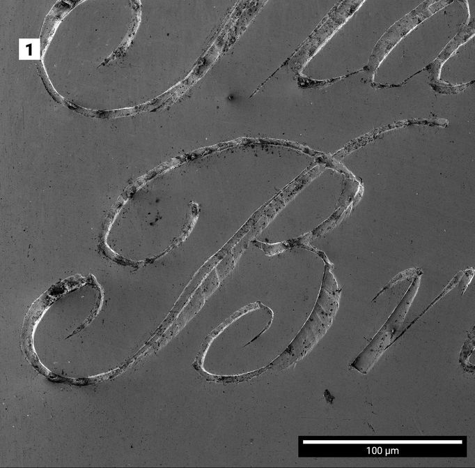 Mikroskopická fotografie detailu rytecké práce: nápis na lžíci.