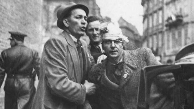 Lidé pomáhají nastoupit do automobilu zraněnému muži v Železné ulici během pražského povstání v květnu 1945.