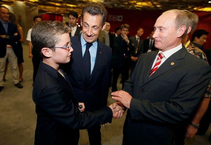 Ze zákulisí zahajovacího ceremoniálu: Louis Sarkozy (vlevo) se zdraví s ruským premiérem Vladimírem Putinem, přihlíží otec Nicolas Sarkozy, prezident Francie.