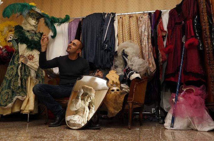 Marco Dilauro gestures next to a mirror with a reflection of his wife Nadia wearing one of his creations, an elaborate costume for the Venice Carnival January 25, 2013. Dilauro, 43, is a tax collector by day, but his real passion is making masks and costumes for the carnival. A resident of Como, northern Italy, he chooses fabrics, ribbons, lace and costume jewellery to make the period costumes after doing extensive research, and wears them at Carnival, which ends on the day before Ash Wednesday. Picture taken January 25, 2013. REUTERS/Alessandro Bianchi (ITALY - Tags: SOCIETY) Published: Led. 27, 2013, 11:29 odp.