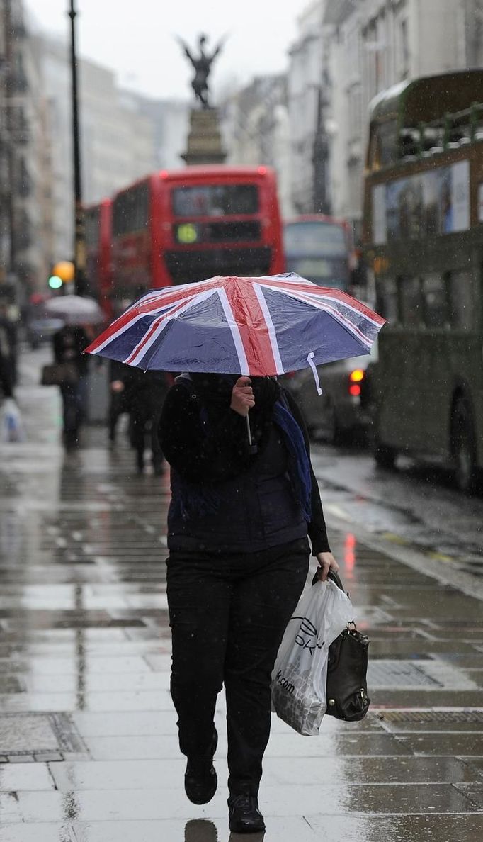 A woman holds an umbrella with a union flag design as she walks in the rain in London in this April 26, 2012 file photo. A quarter of a million rain ponchos, an army of volunteers equipped with umbrellas and rain jackets, and five dedicated weather forecasters - it must be a British Olympics. Planning any outdoor event during the unpredictable British summer, renowned for its potential to throw up more rainy spells than sunshine, requires drawing up contingency plans and keeping a close eye on the weather. REUTERS/Paul Hackett/Files (BRITAIN - Tags: SOCIETY ENVIRONMENT SPORT OLYMPICS) Published: Čer. 27, 2012, 6:49 dop.