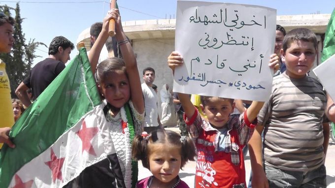 Proti režimu syrského prezidenta Bašára Asada demonstrují i malé děti. Snímek pochází z 29. června z městečka Al-Kasten poblíž Idlíbu. Na transparentu je nápis: "Bratři mučedníci, vyčkejte, přicházím."