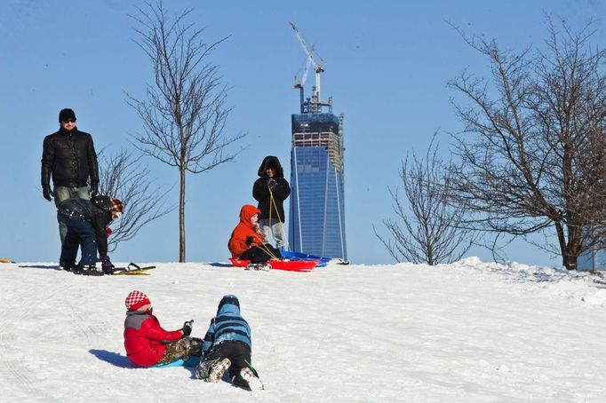 Children ride down a hill on a toboggan as One World Trade Center is seen in Jersey City, New Jersey, February 9, 2013. A blizzard packing hurricane-force winds pummelled the northeastern United States on Saturday, killing at least one person, leaving about 600,000 customers without power and disrupting thousands of flights. REUTERS/Eduardo Munoz (UNITED STATES - Tags: ENVIRONMENT DISASTER) Published: Úno. 10, 2013, 12:49 dop.