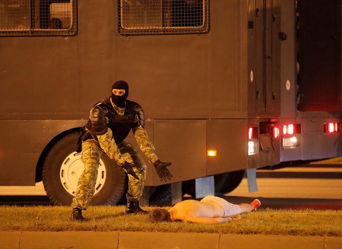 Běloruský policista ukazuje na tělo zraněného demonstranta, který zůstal ležet po střetu s těžkooděnci na zemi.