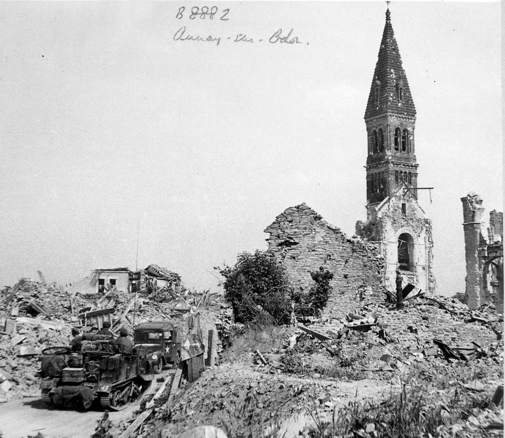 A bulldozer clears a path near the tower of a destroyed church, the only structure left standing after Allied bombing raids in Aunay-Sur-Odon