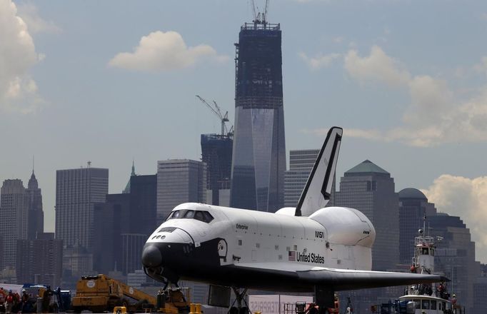 The Space Shuttle Enterprise passes lower Manhattan and the still under construction 1 World Trade Center tower (C) as it rides on a barge in New York harbor, June 6, 2012. The Space Shuttle Enterprise was being moved up the Hudson River to be placed at the Intrepid Sea, Air and Space Museum. REUTERS/Mike Segar (UNITED STATES - Tags: TRANSPORT SCIENCE TECHNOLOGY) Published: Čer. 6, 2012, 3:53 odp.