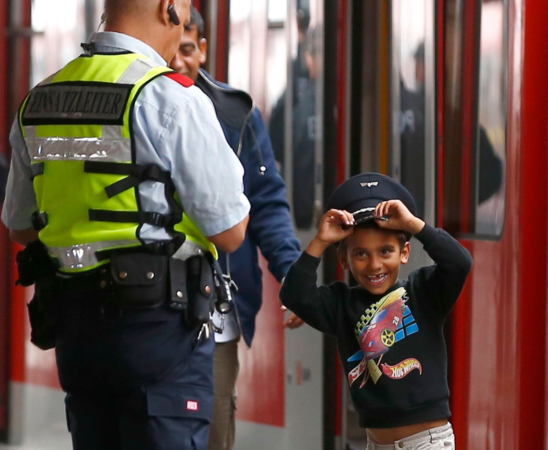 uprchlíci Migrant boy tries on Bahn security officer's cap after arriving by train from Salzberg at station in Munich