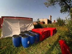 Mobilní dezinfekční sprchy v Netřebech. Použité roztoky a odpadní vodu odváží v červených nadržích specializovaná firma. Vše, co mají pracovníci v drůbežárně na sobě, se vyhazuje do modrých barelů ke spálení.