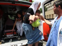 I toto je realita v Izraeli: Matka odnáší lehce zranění dítě, které poranily úlomky ostřelovaného domu, do nemocnice.