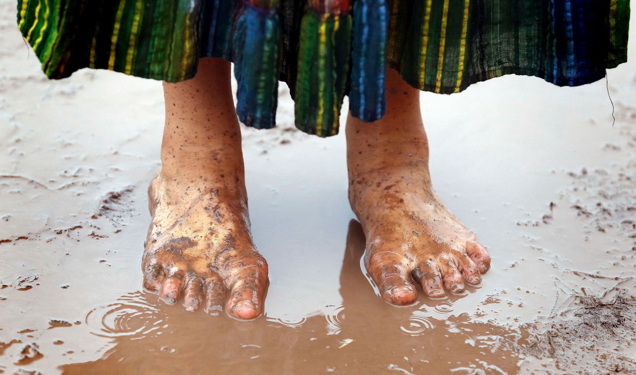A festival goer stands barefoot in a muddy puddle at Worthy Farm in Somerset, on the third day of the Glastonbury music festival