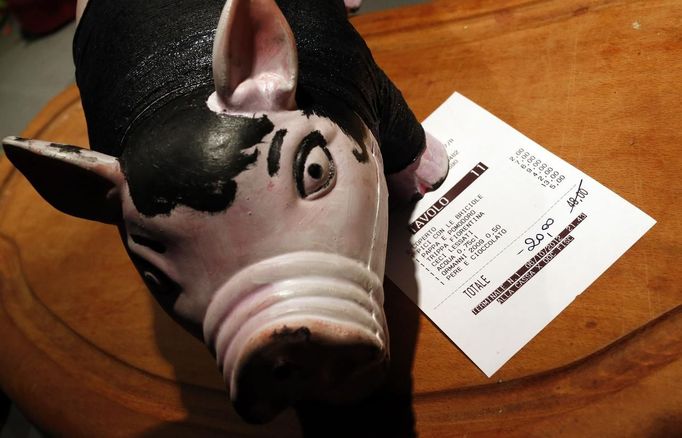 A plastic pig figurine is placed over a ticket showing a discount of 20 euros after a barter with bottles of liquor are exchanged for a meal at the "L'e'Maiala" restaurant in Florence October 6, 2012. At walking distance from the tourist cafeterias around Palazzo Vecchio, Faggioli and her husband Frank are busy bartering wine and potatoes for a meal of Tuscan "pici" pasta with pork sauce. The neighbourly couple have recently launched a 40-seat restaurant in Florence that allows customers to exchange vegetables and used goods for a traditional Tuscan dinner, in a way to encourage people to dine out despite the recession. Picture taken October 6, 2012. To match story ITALY-BARTER/ REUTERS/Alessandro Bianchi (ITALY - Tags: SOCIETY BUSINESS) Published: Říj. 10, 2012, 9:31 dop.