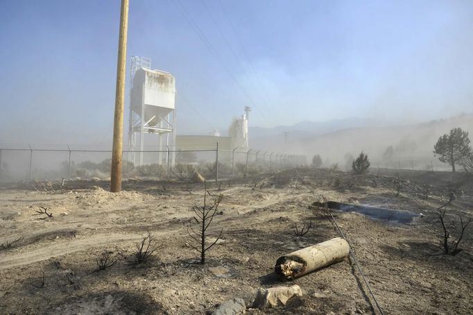 A telephone pole, damaged from the so-called Dump Fire, smoulders on the ground outside of an explosives plant near Saratoga Springs, Utah, June 23, 2012. A raging Utah brush fire ignited by target shooting in dry grass has forced some 8,000 people from their homes in two small communities since June 22 as high winds fanned flames toward a nearby explosives factory, authorities said. REUTERS/Jeff McGrath (UNITED STATES - Tags: ENVIRONMENT DISASTER) Published: Čer. 24, 2012, 2:02 dop.