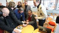 Následuje krátká autogramiáda. Vedle kandidáta stojí jeho tiskový mluvčí. Jeden ze členů volebního týmu, který Karla na jeho cestě Moravou doprovází.