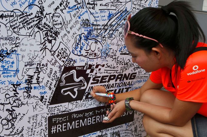 A woman writes on a wall dedicated to the passengers of the missing Malaysia Airlines flight MH370 before the Malaysian F1 Grand Prix at Sepang International Circuit outs