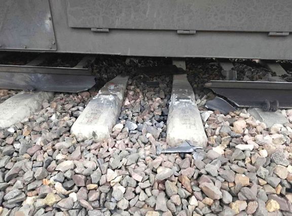 Poškozená železniční trať s roztříštěnými betonovými pražci a zdeformovaným úsekem ocelové kolejnice. Listopad 2025.