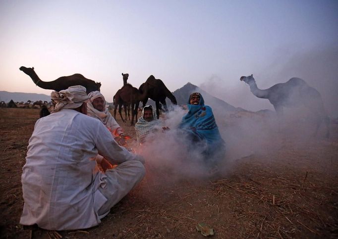 Camel herders sit around a bonfire to warm themselves as they wait for customers at Pushkar Fair in the desert Indian state of Rajasthan November 22, 2012. Many international and domestic tourists throng to Pushkar to witness one of the most colourful and popular fairs in India. Thousands of animals, mainly camels, are brought to the fair to be sold and traded. REUTERS/Danish Siddiqui (INDIA - Tags: ANIMALS SOCIETY) Published: Lis. 22, 2012, 5:29 odp.