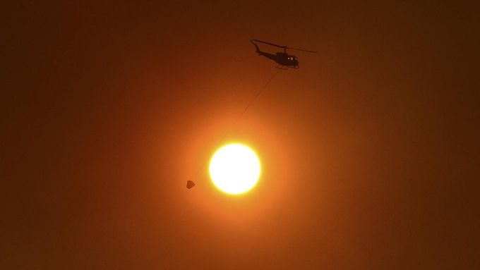 Helicopter with bucket used for carrying water for dropping onto bushfires, flies past the sun as it is obscured by smoke in western Sydney